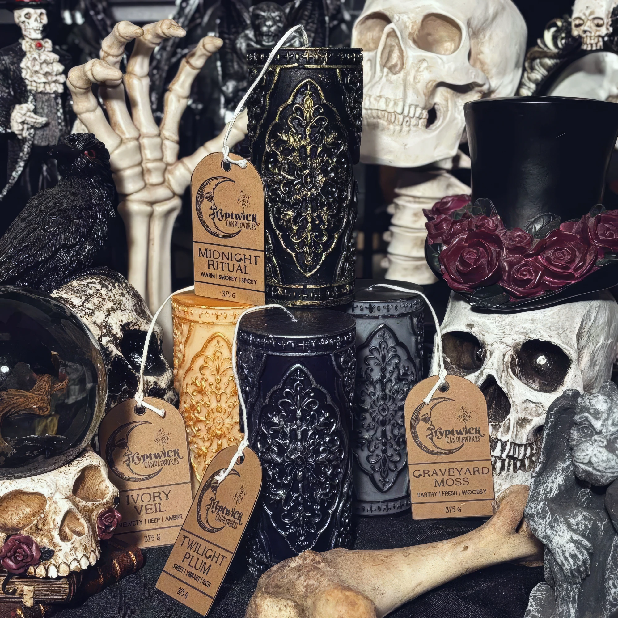 Four carved gothic pillar candles — black-and-gold, ivory, black and grey — each ringed with raised tracery and hung with a Cryptwick kraft tag, staged among skulls, roses and a crystal ball.